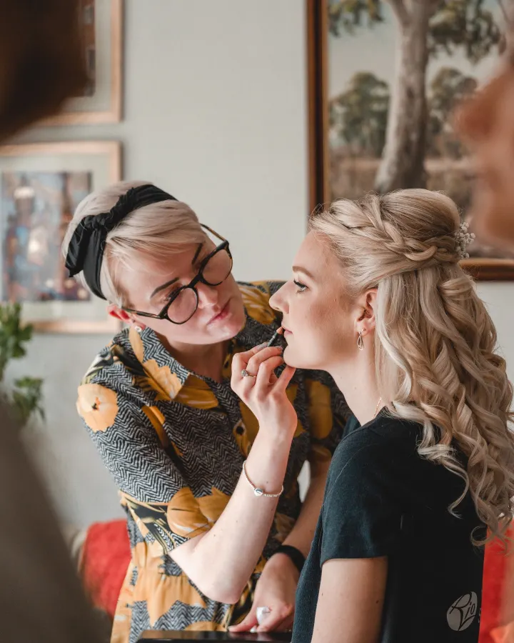 Our make-up artist lining the lips of a bride with half-up curls and a braided crown with gypsophila