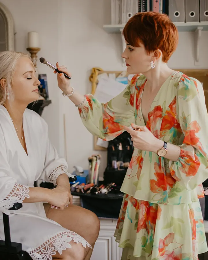 Our make-up artist powdering a blonde bride whose low textured updo has a sprig of gypsophila