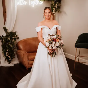Full-length bride in an off-shoulder satin gown with an autumn rose bouquet