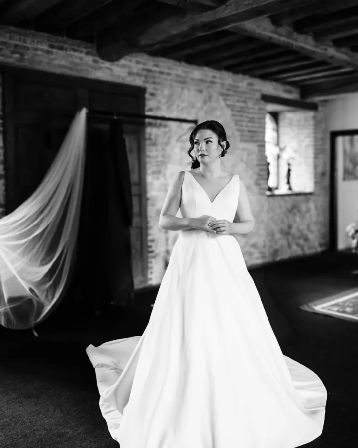 Black-and-white portrait of a bride in a satin gown, her hair in a sleek low bun with soft tendrils and a long veil