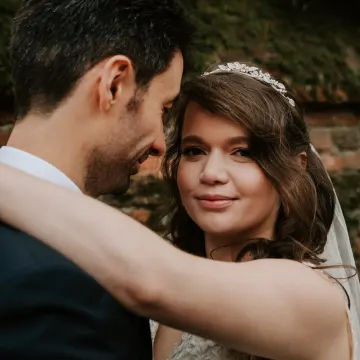 The tiara bride embracing her groom by a brick wall, with half-up curls and soft glam