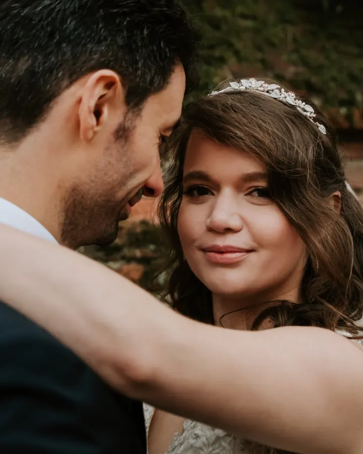 The tiara bride embracing her groom by a brick wall, with half-up curls and soft glam