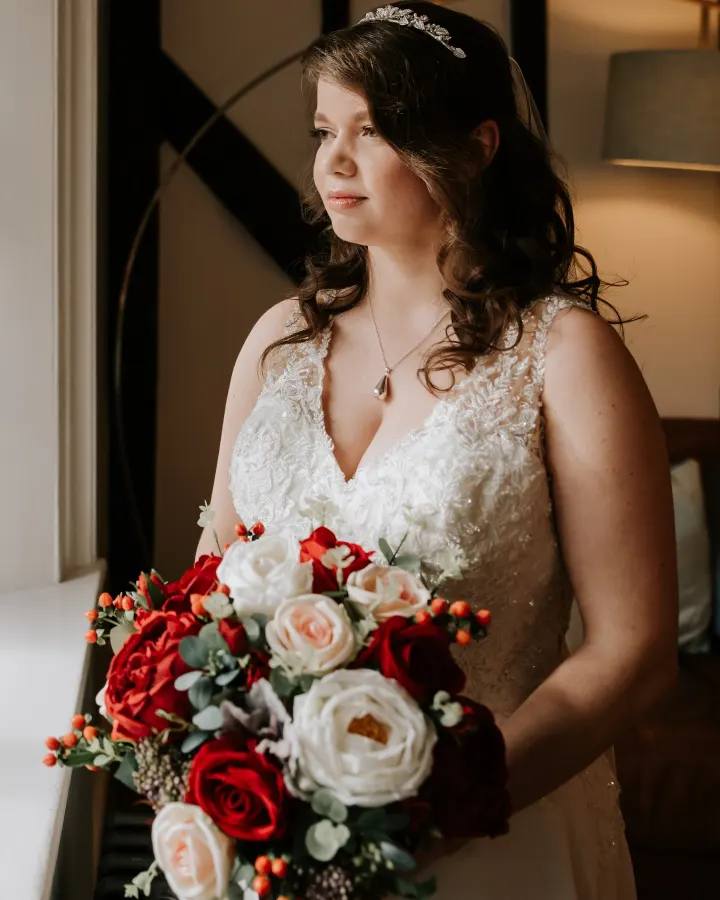 Bride in window light with a rose bouquet: half-up soft brunette curls, a crystal leaf tiara and luminous natural make-up