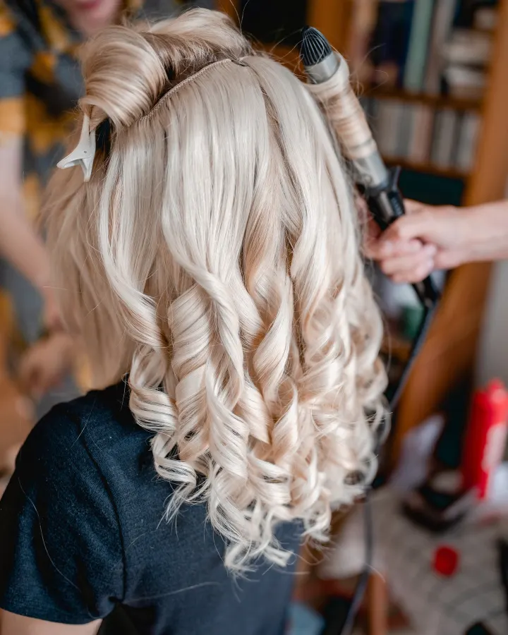 Sectioned blonde hair being curled with tongs into glossy barrel curls