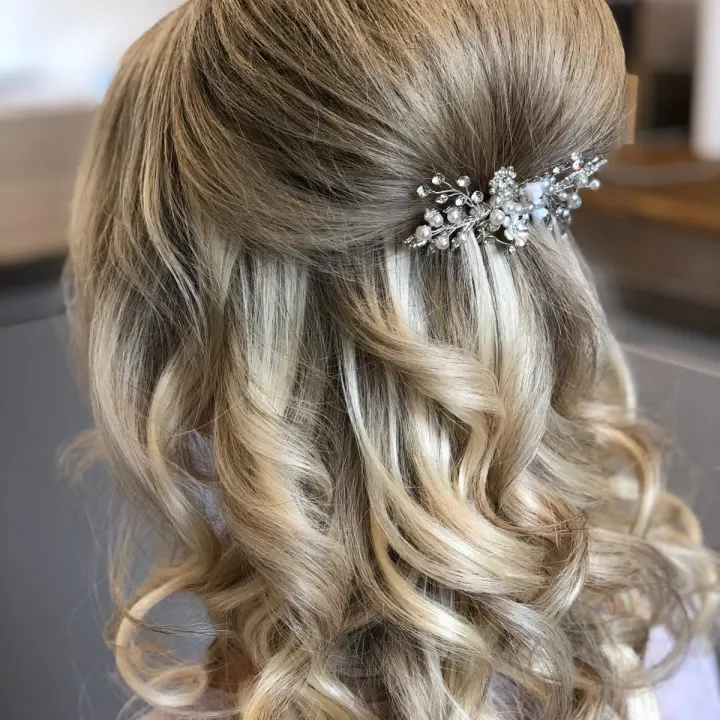 Back view of blonde half-up hair with a raised crown, a crystal-and-pearl comb and bouncy curls