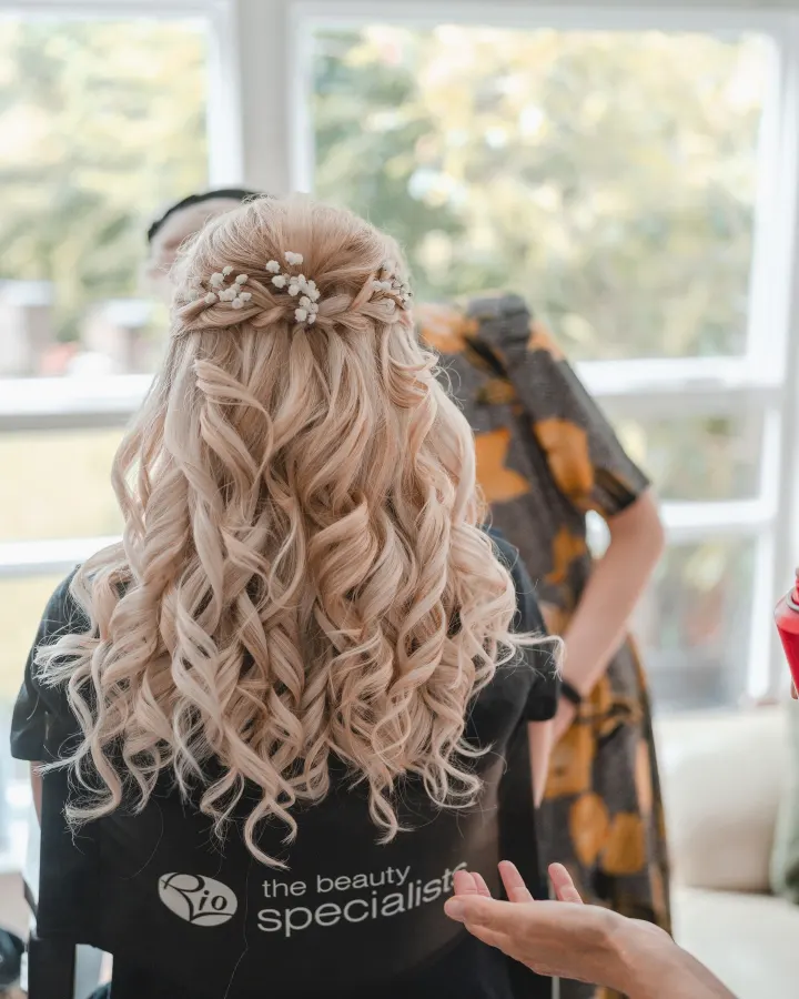 Back view of long blonde hair half-up, with a braided crown and gypsophila over full ringlets