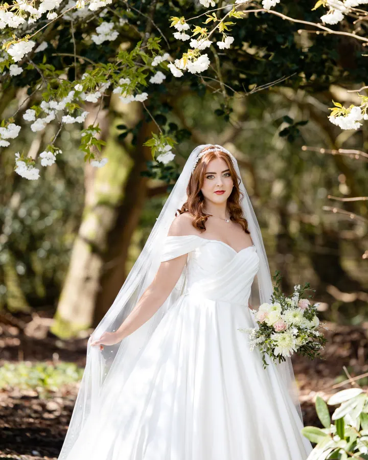 Bride under a blossoming cherry tree: loose glossy waves under a pearl headband and a pearl-scattered veil