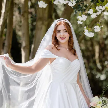 The blossom-tree bride smiling, her veil swept out: glossy waves, a pearl headband and a red lip