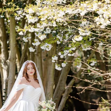 Bride under a canopy of white blossom, eyes lowered