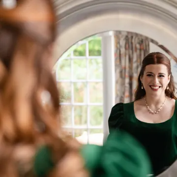 Smiling at the mirror in green velvet: half-up auburn waves with pearl pins
