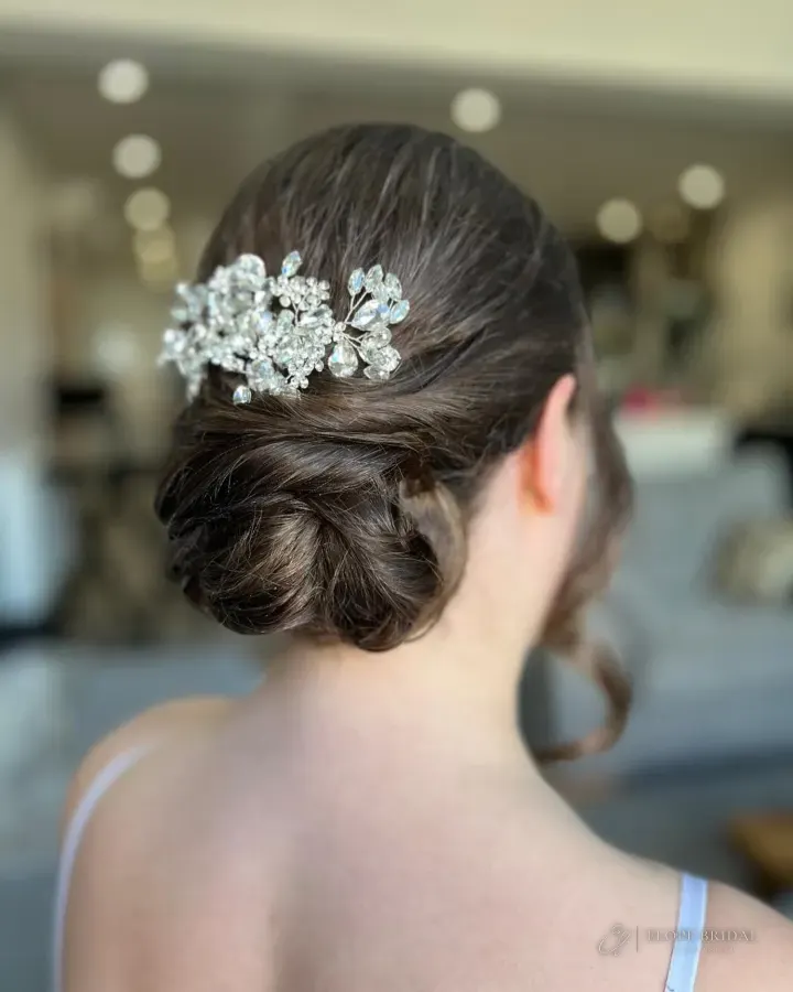 A sleek low twisted chignon with a large crystal comb and one loose curled tendril