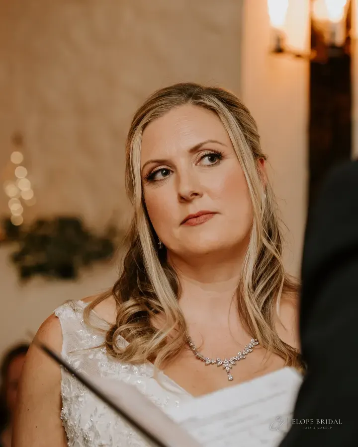 Bride during her vows: half-up blonde waves, a champagne shimmer lid and a terracotta-nude lip